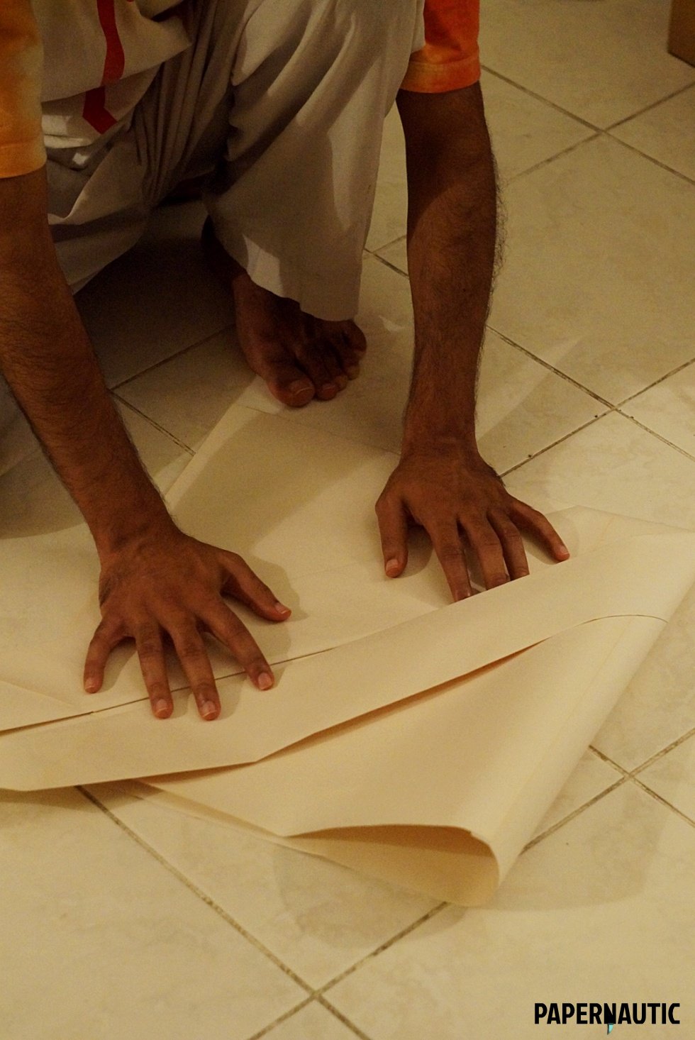 Large sheet of paper being folded into a samurai paper hat on the floor.